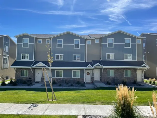 Contemporary townhome exterior featuring multi-toned siding, stone accents, white trim, and a manicured lawn