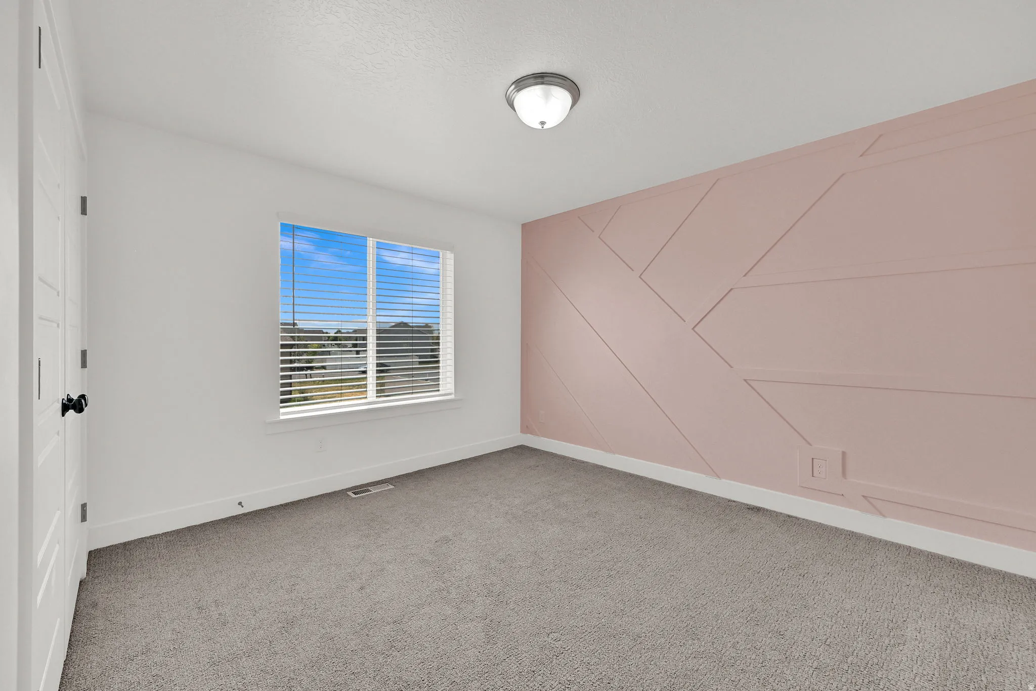 Geometric accent wall, wall-to-wall carpeting, white trim, single window, and a flush-mount light fixture