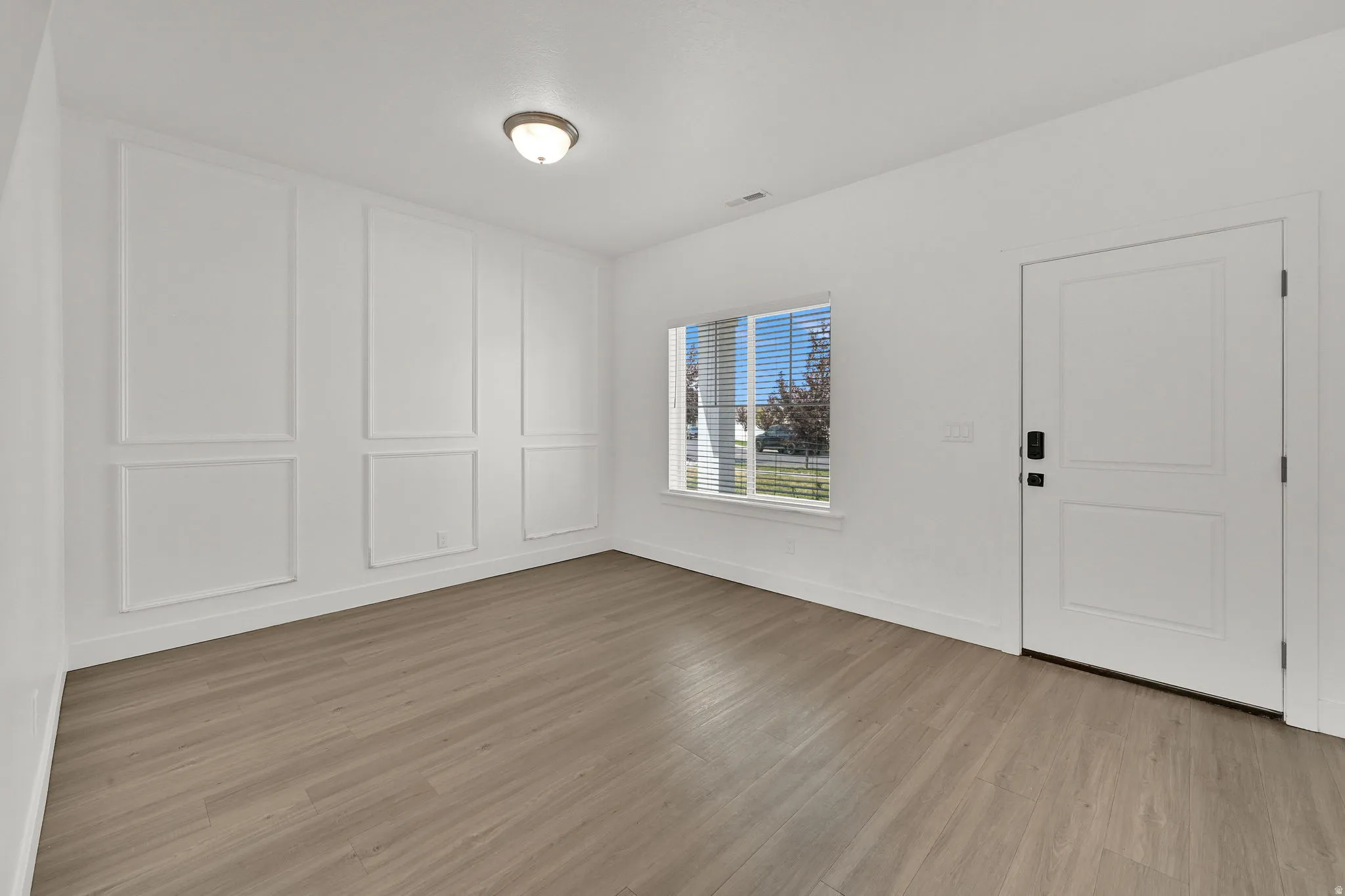 Interior space featuring wood-finish flooring, a decorative accent wall with panel molding, a recessed window, and a white paneled door with contemporary hardware