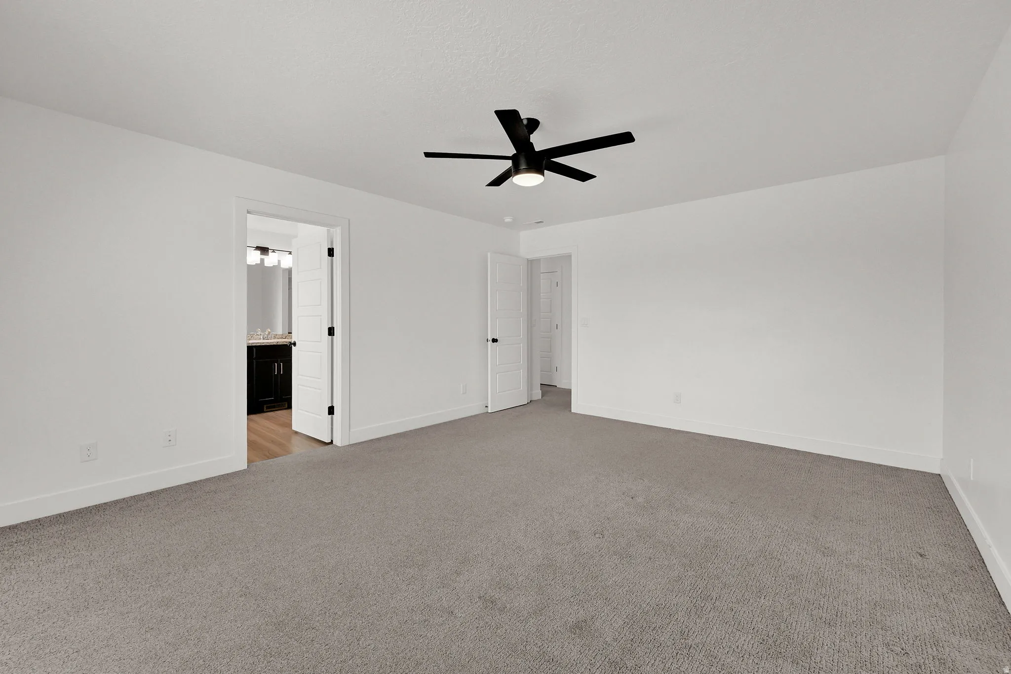 White walls with gray carpeting, featuring a matte black ceiling fan