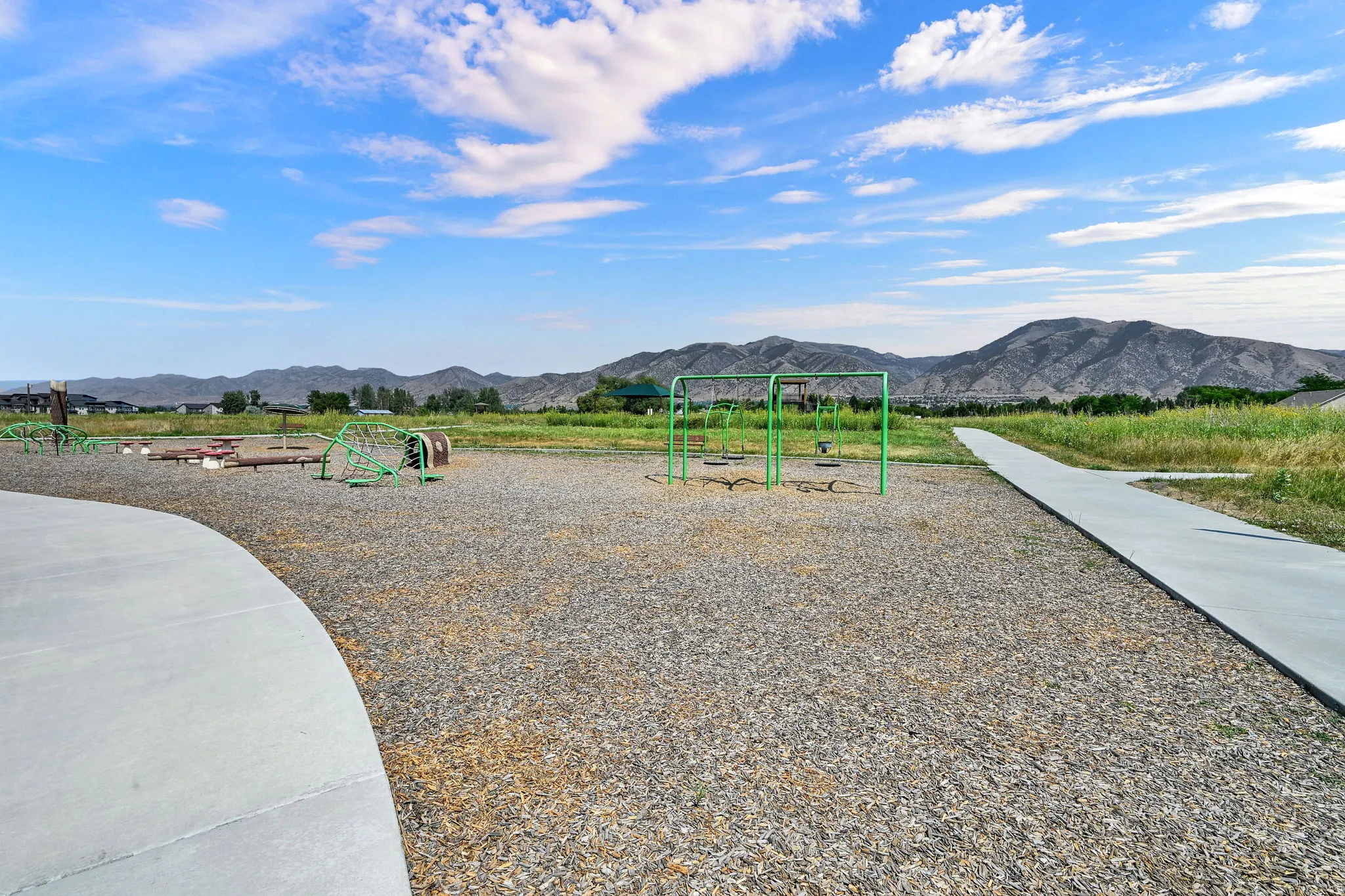 Community playground with multiple play structures, a wide concrete pathway, and distant mountain scenery