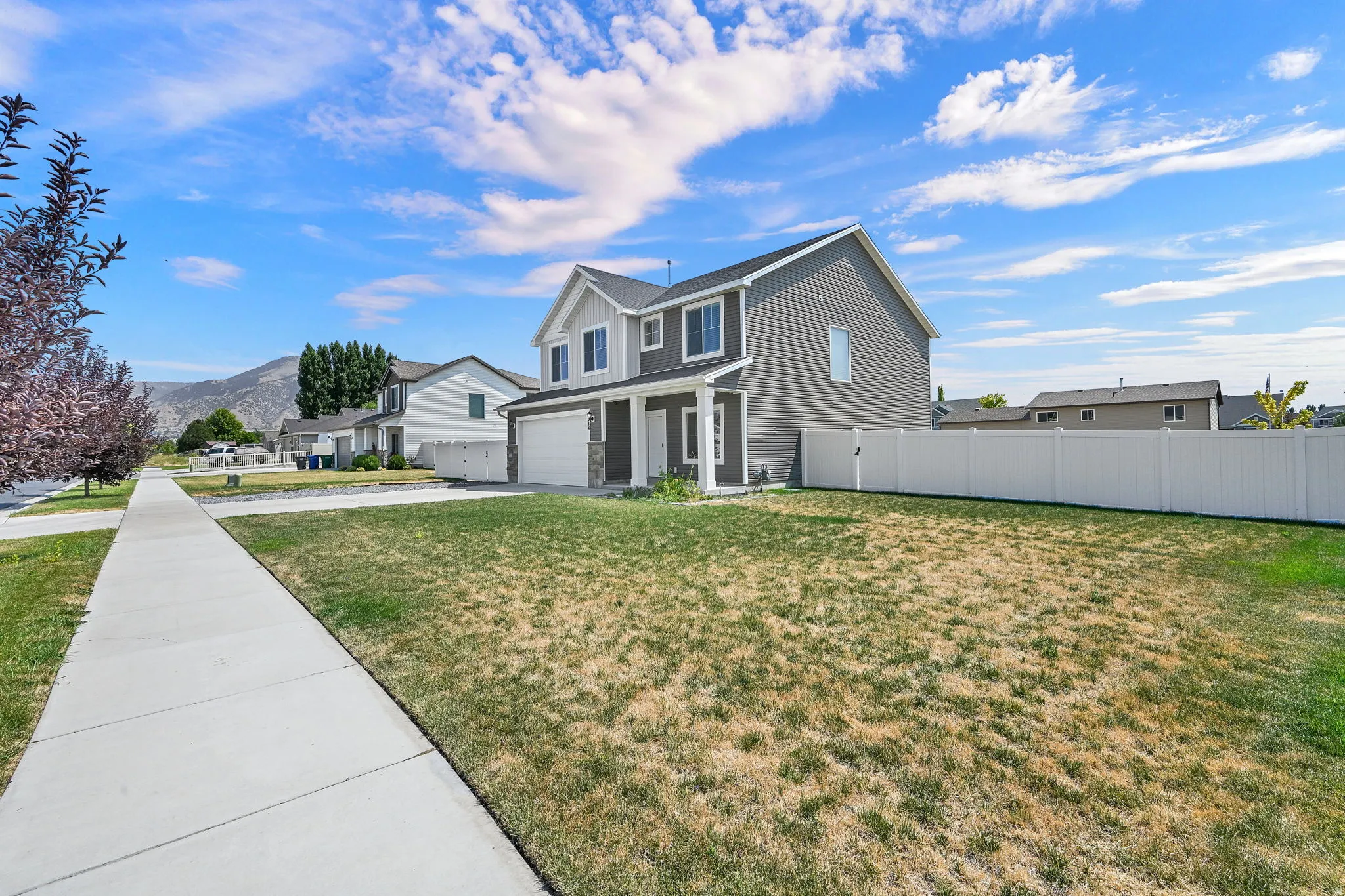 Two-story residence featuring a two-car garage, gray siding, white trim, and a white privacy fence