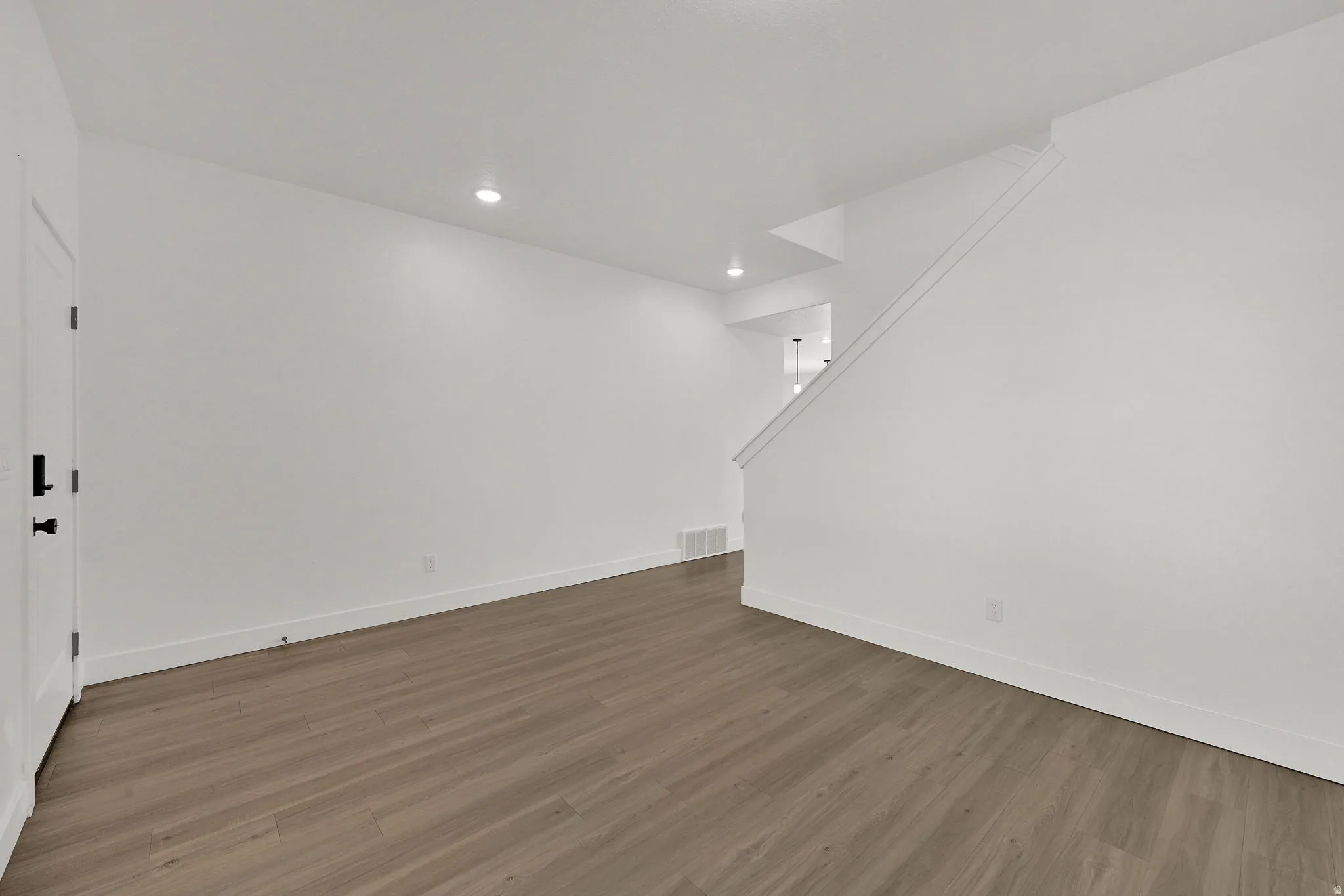 Wood-finish flooring throughout, bright white walls, recessed ceiling lights, and modern white interior doors with black hardware