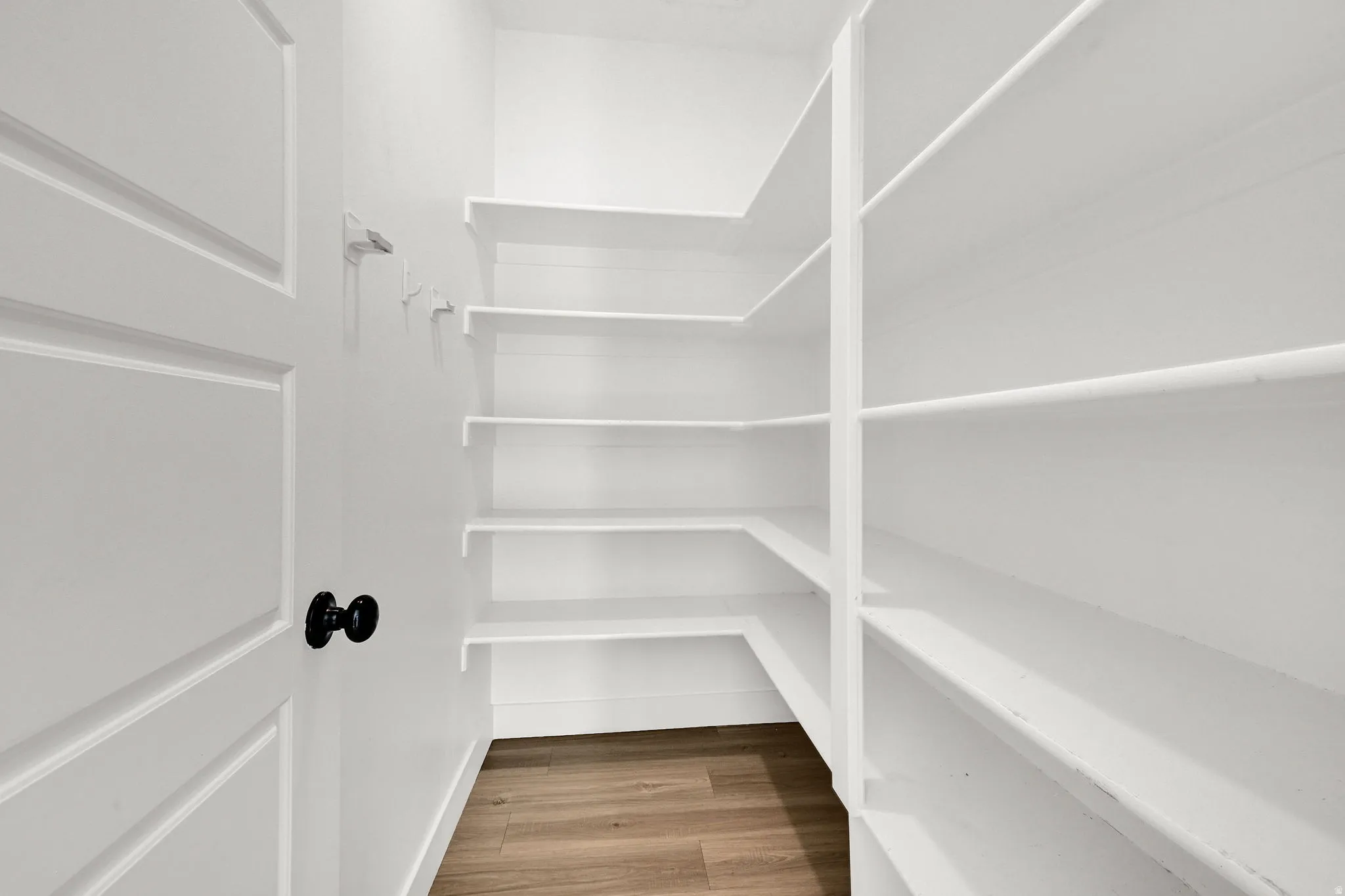 White door with black hardware, white walls, built-in white shelving, and wood-finish flooring