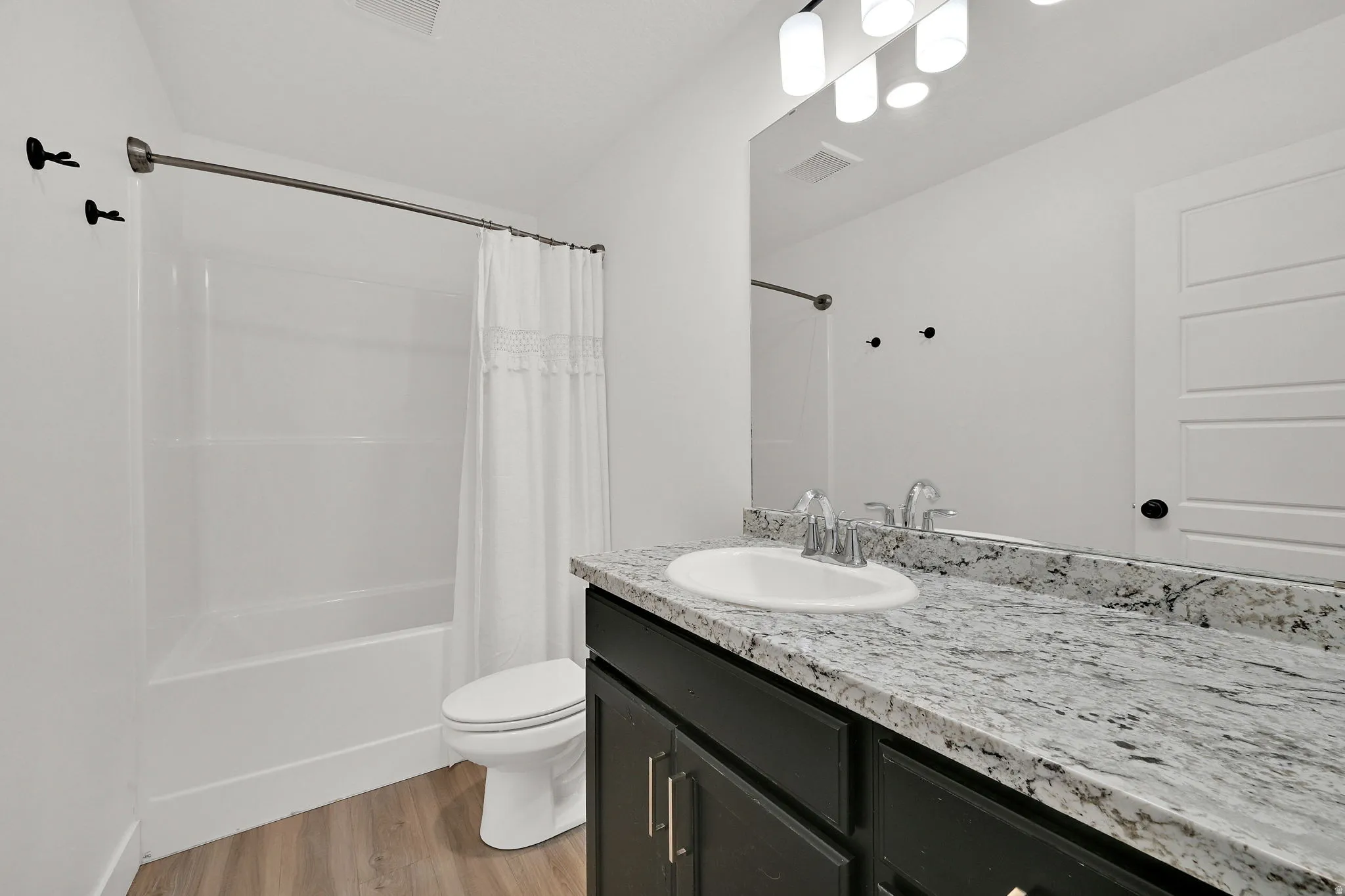 Wood-finish flooring, dark cabinetry, and a light-colored countertop with an undermount sink