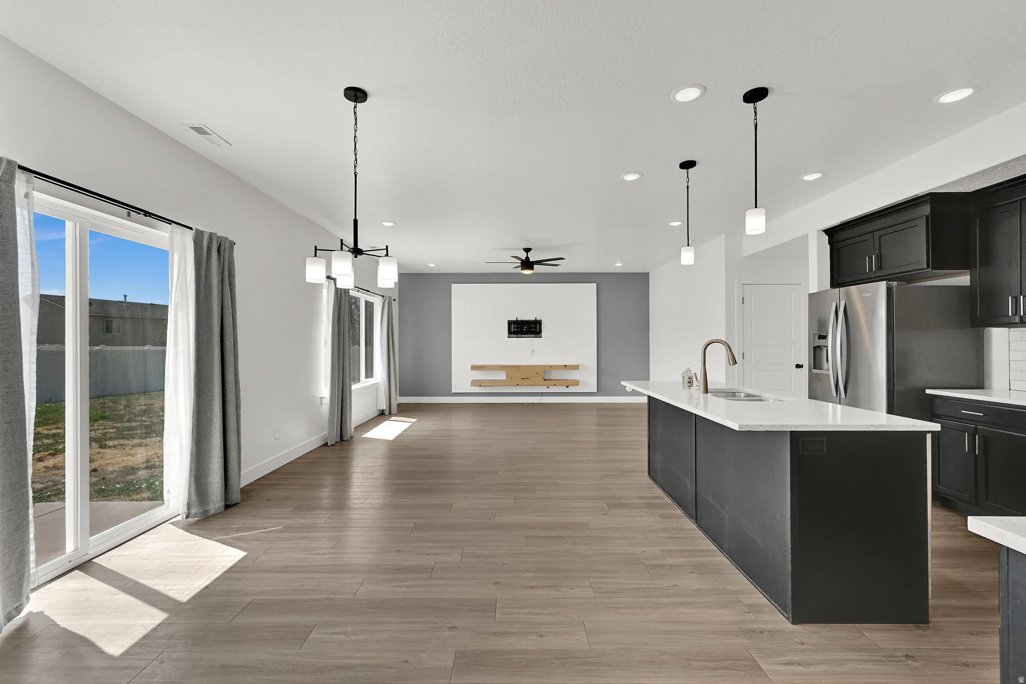 Open-concept living space featuring wood-finish flooring, a kitchen island with a white countertop, dark cabinetry, and stainless steel appliances