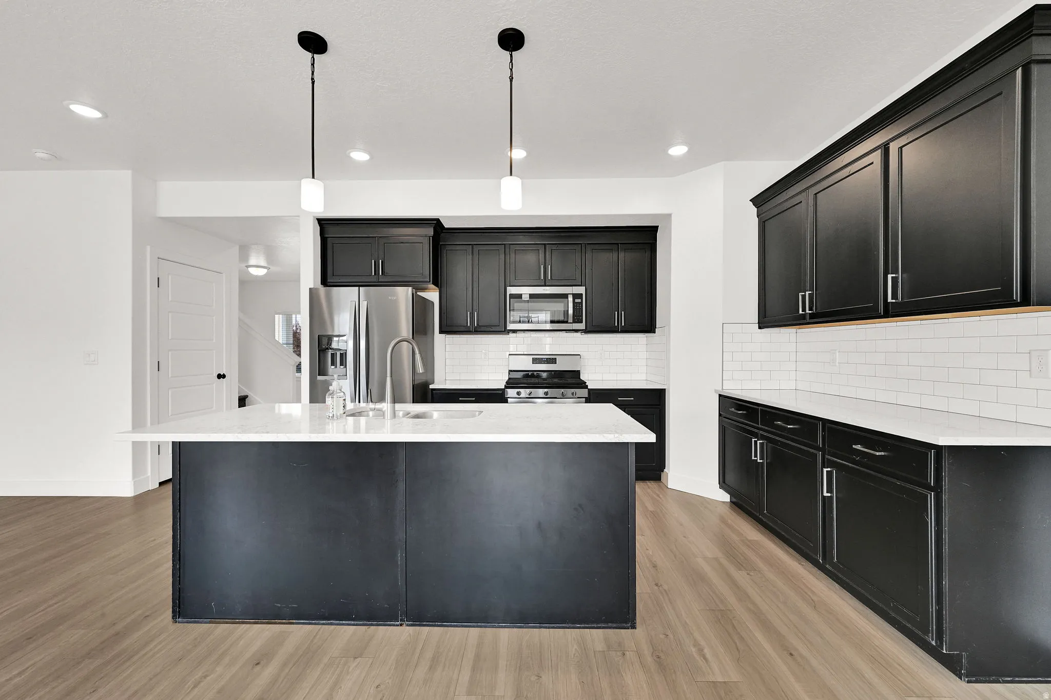 Kitchen featuring dark cabinetry, stainless steel appliances, a center island with sink, subway tile backsplash, and light wood-finish flooring