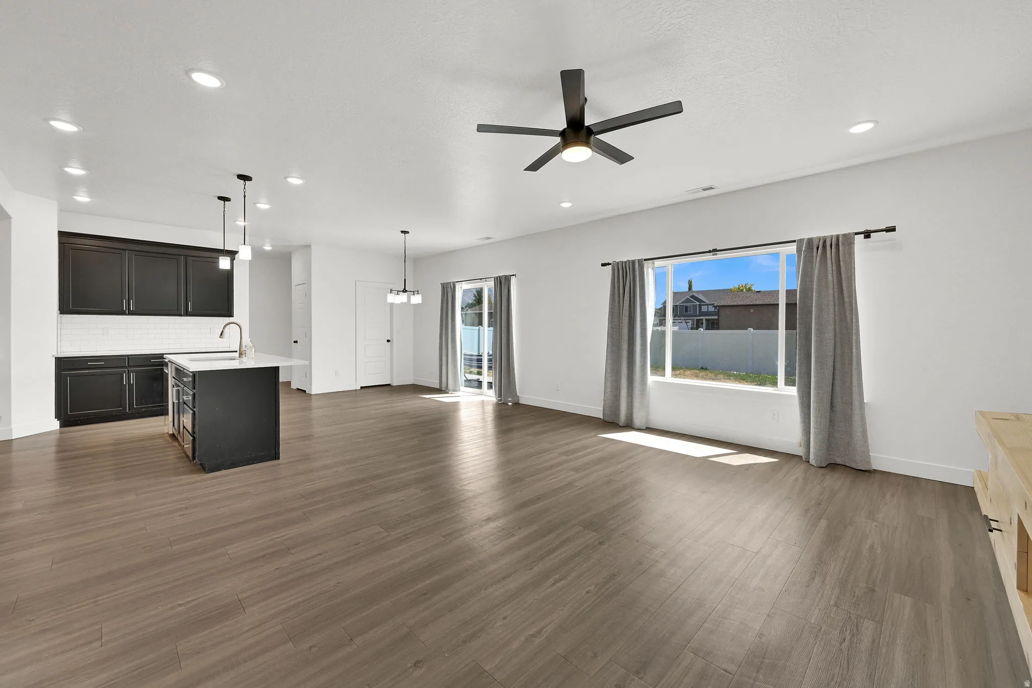 Open-concept living area featuring wood-finish flooring, a kitchen island with a sink, pendant lighting, and a sliding glass door