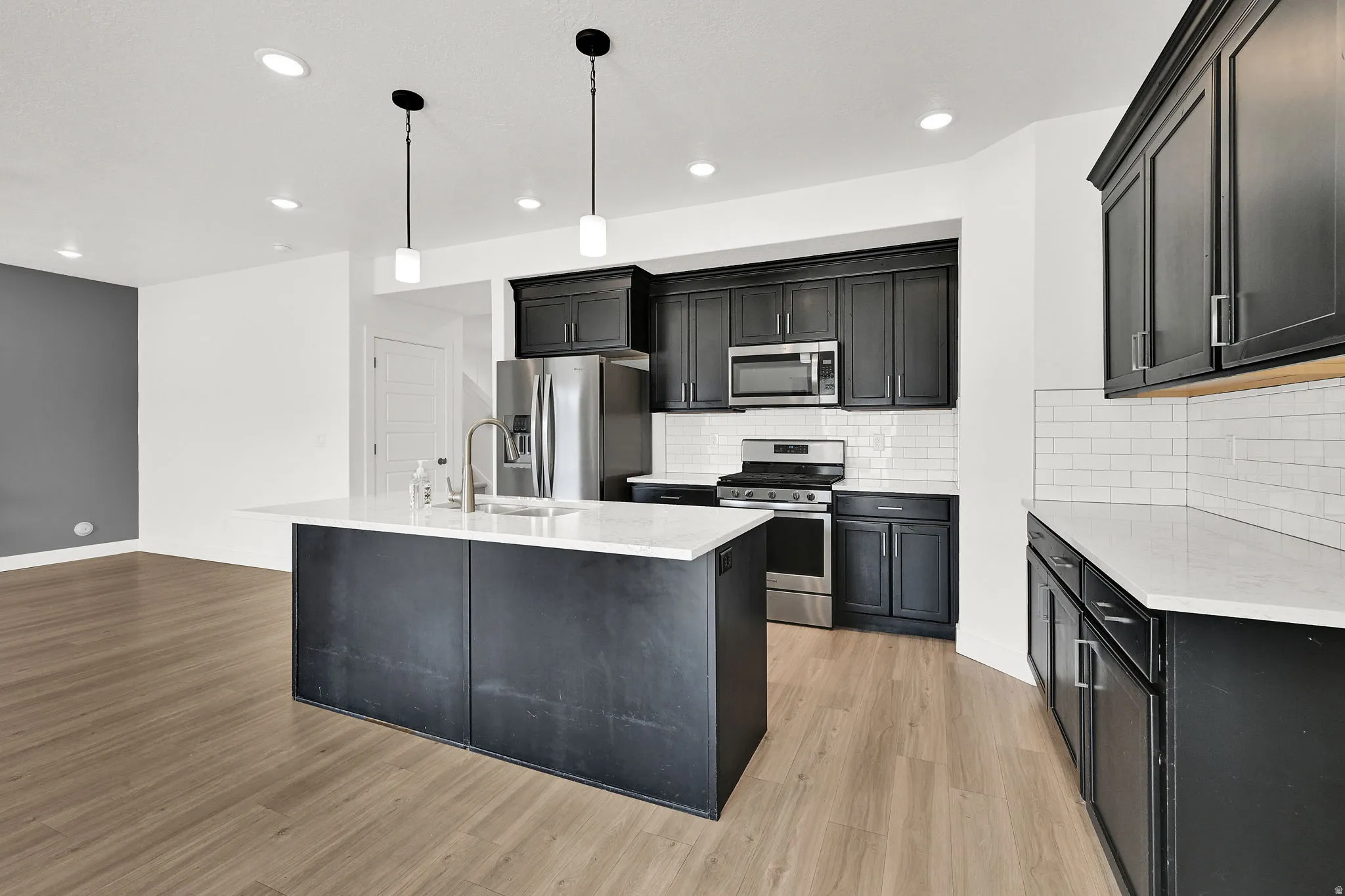 Kitchen featuring dark cabinetry, stainless steel appliances, a center island with a sink, white countertops, and subway tile backsplash