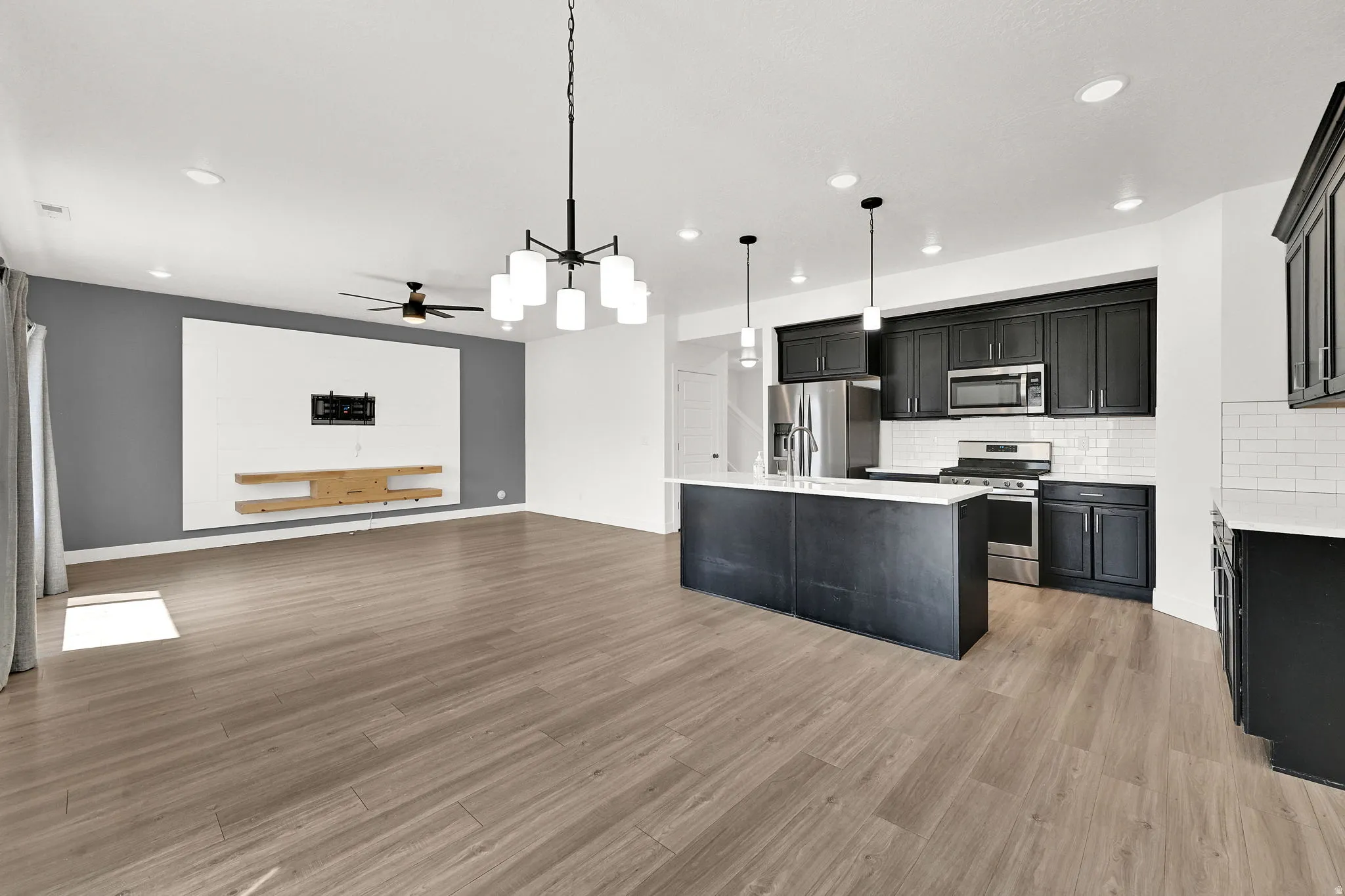 Open-concept living space featuring wood-finish flooring, a modern black chandelier, and recessed lighting