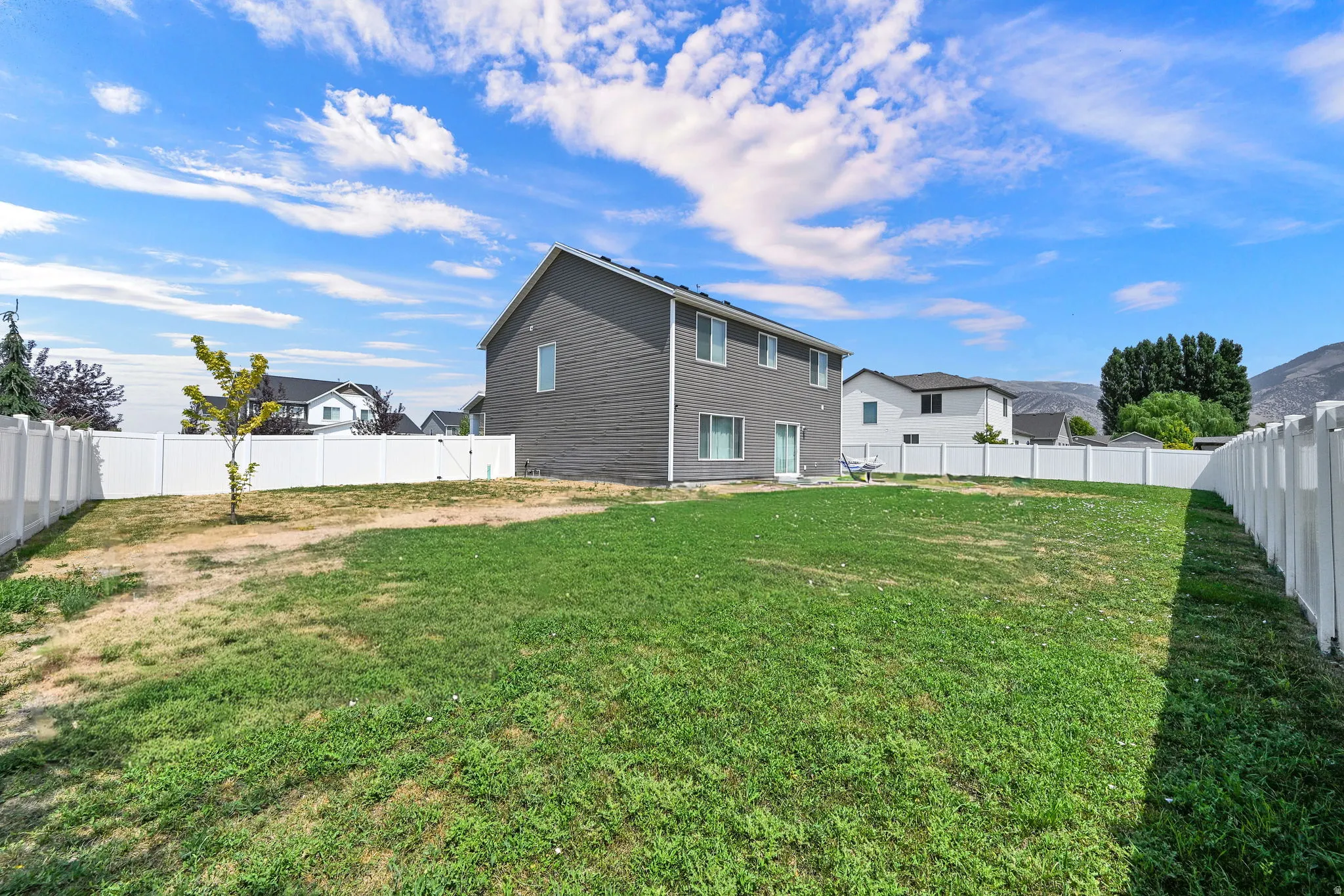 Expansive backyard with mature landscaping and level lawn space, enclosed by white vinyl fencing