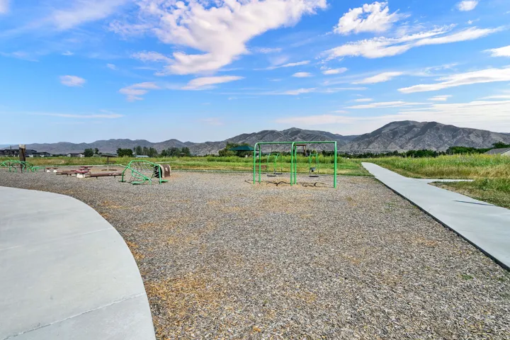 Community playground with multiple play structures, a wide concrete pathway, and distant mountain scenery