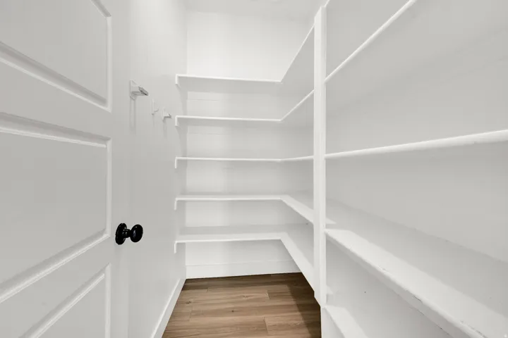 White door with black hardware, white walls, built-in white shelving, and wood-finish flooring