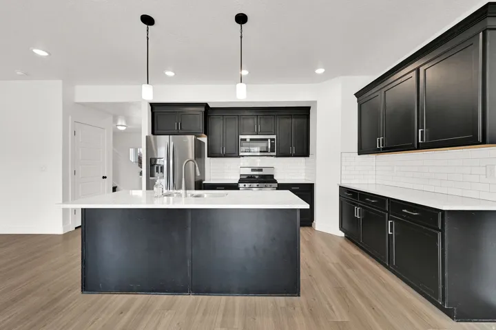 Kitchen featuring dark cabinetry, stainless steel appliances, a center island with sink, subway tile backsplash, and light wood-finish flooring