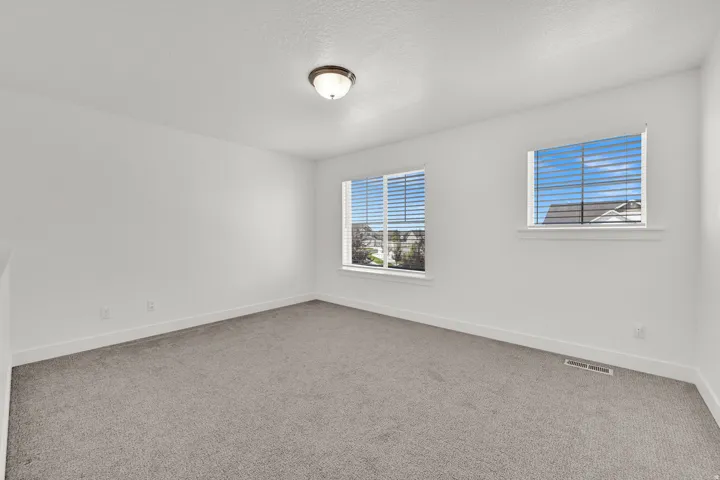 Neutral-toned carpeting, white walls, two windows with blinds, and a flush mount ceiling light fixture