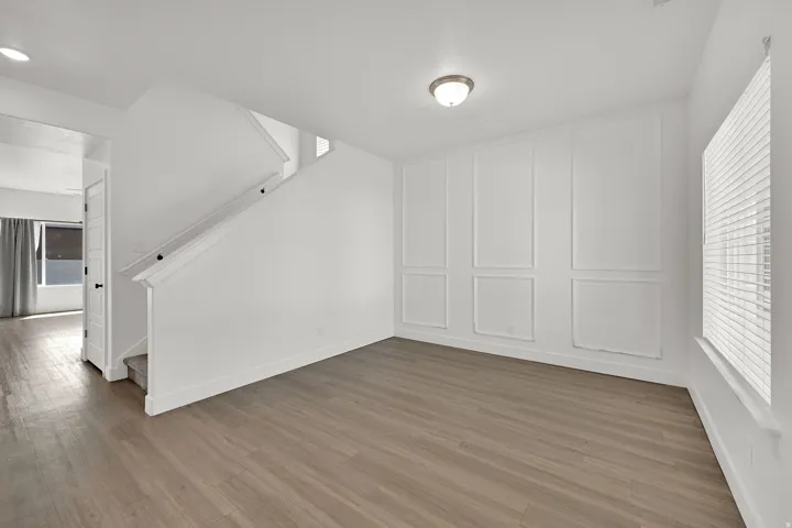 Wood-finish flooring, accent wall paneling, flush mount lighting, staircase with white railing, and window with blinds