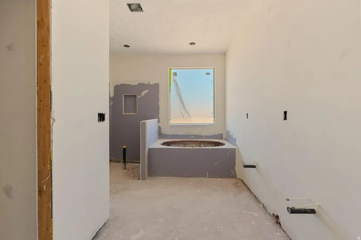 Built-in soaking tub with surrounding wall, recessed niche, and flush-mounted ceiling lights