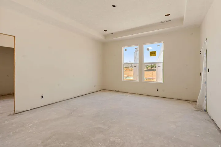 Recessed lighting, tray ceiling, two windows, and an unfinished concrete floor