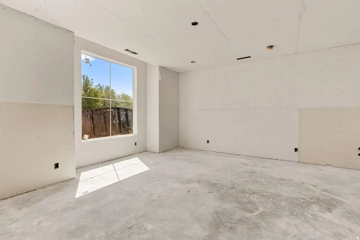Spacious room with large multi-pane window, exposed concrete flooring, recessed lighting, and unfinished drywall