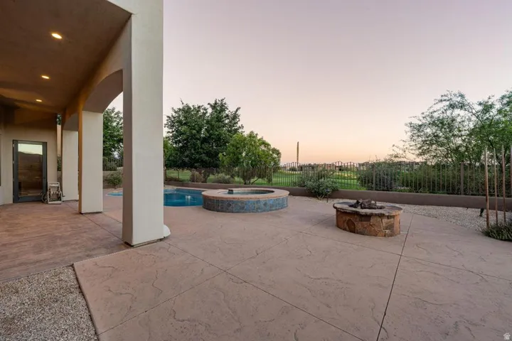 Expansive stamped concrete patio with recessed lighting, a built-in fire pit, and an integrated pool and spa feature