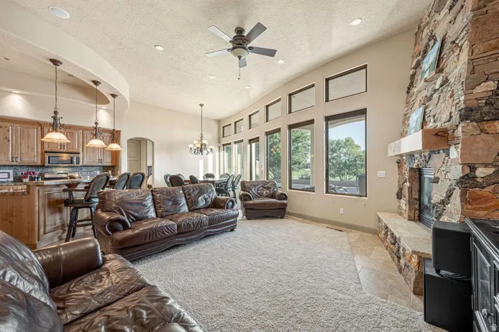 Vaulted ceiling with recessed lighting, stone-clad fireplace with hearth, built-in kitchen cabinetry with pendant lighting, and multiple large windows