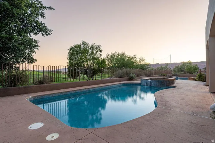Freeform swimming pool with an integrated spa, expansive concrete decking, and a perimeter fence