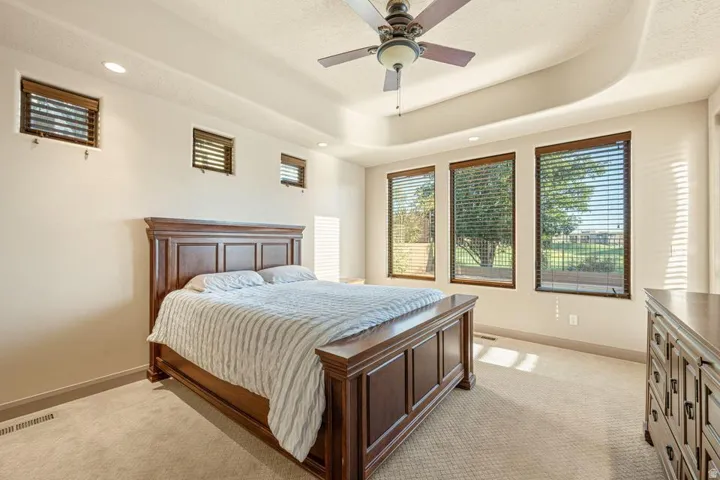 Tray ceiling, recessed lighting, ceiling fan, three vertical windows, and carpet flooring