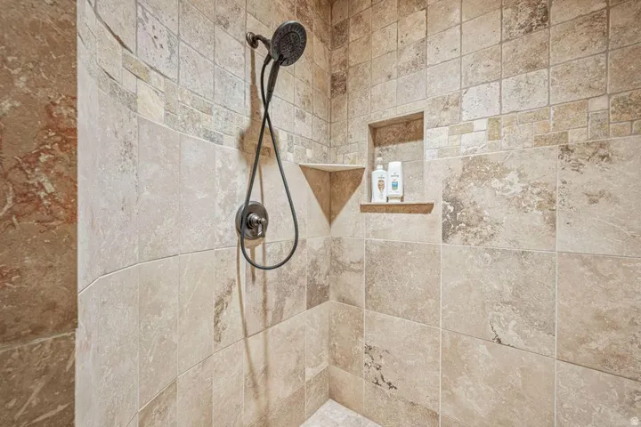 Tiled shower enclosure featuring a handheld showerhead, built-in corner shelf, and recessed niche