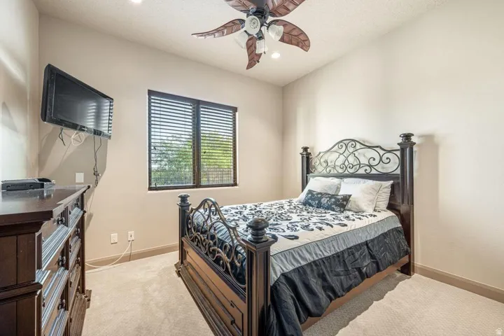 Spacious secondary bedroom featuring an ornamental wrought iron bed frame, neutral carpet flooring, and abundant natural light from dual windows with plantation shutters