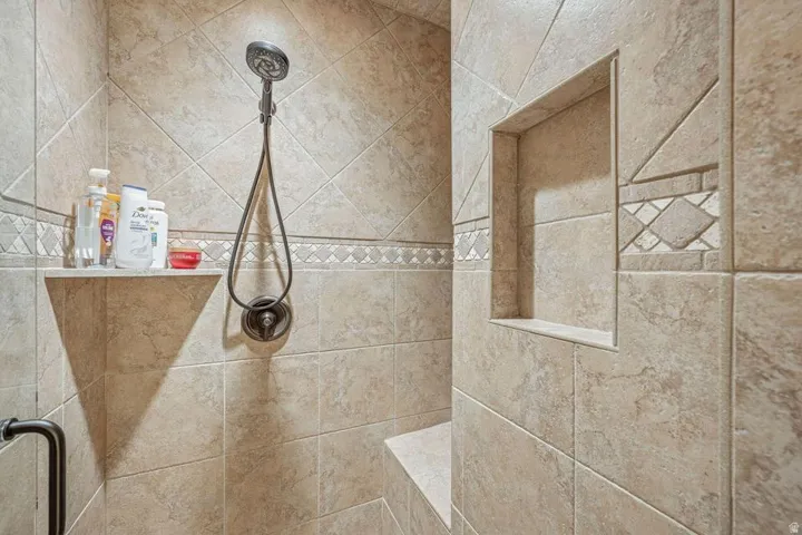 Tiled shower with handheld shower fixture, built-in corner shelf, integrated bench, and decorative accent tiles