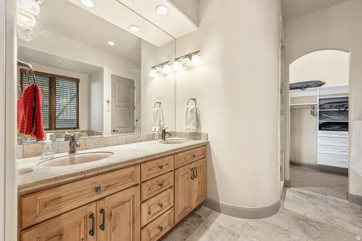 Spa-inspired primary bathroom showcasing a dual-sink vanity with warm wood cabinetry, stone countertops, and polished nickel hardware