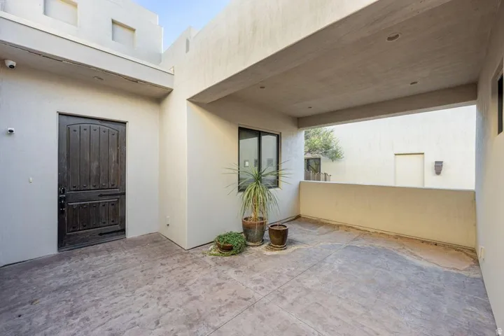 Covered patio with recessed lighting, stucco exterior, and a solid wood entry door with iron hardware