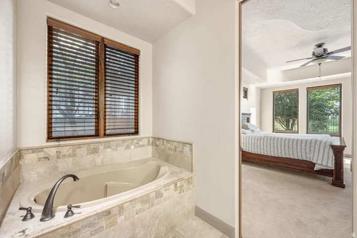 Built-in soaking tub with tile surround, wood-framed windows with blinds, and recessed lighting
