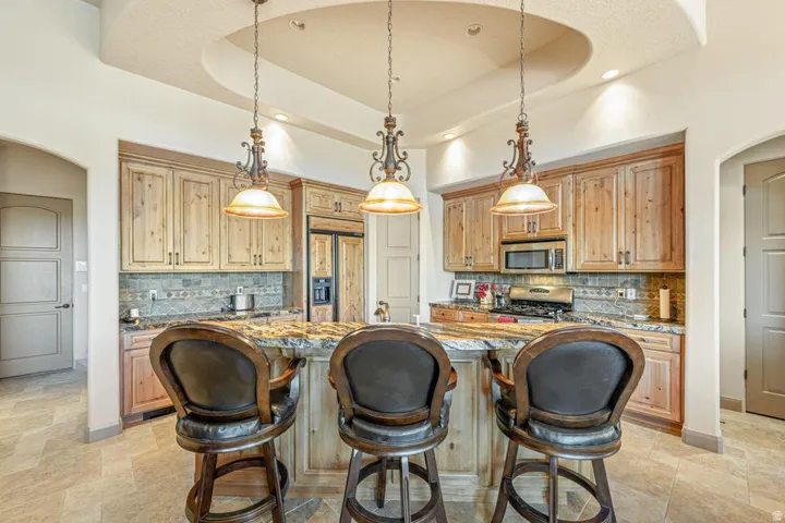 Kitchen island with a stone countertop, three pendant light fixtures, wood cabinetry, stainless steel appliances, and tile flooring