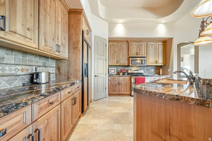 Kitchen featuring wood cabinetry, stone countertops, built-in appliances, a tile backsplash, and tile flooring