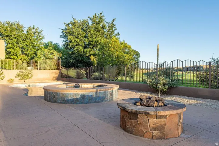 Stained concrete patio featuring a tiled spa, adjacent swimming pool, and stone-clad fire pit