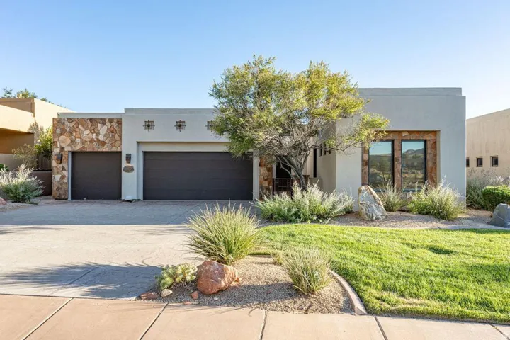 Stucco exterior with stone accents, two-car garage, established front landscaping, and a concrete driveway