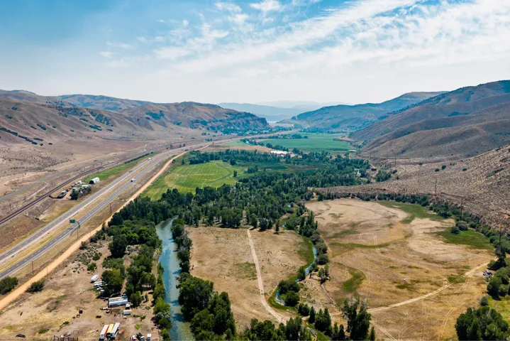 Expansive land featuring a winding river, mature trees, open fields, and surrounding mountainous terrain