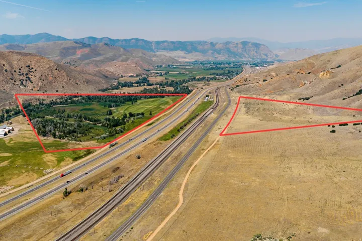 Expansive land parcels with natural terrain, adjacent to highway infrastructure, and framed by distant mountainous landscapes