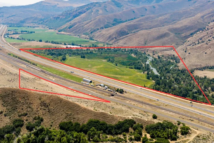 Expansive acreage bordered by a river and mature trees, featuring a flat, open land area