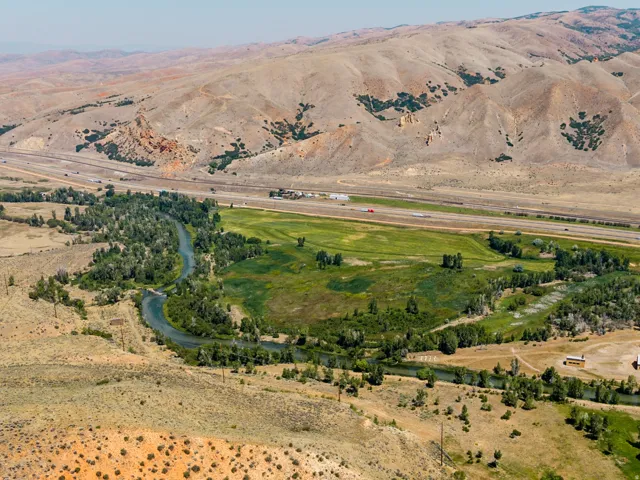 Expansive property featuring a curving river, lush green fields, mature trees, and mountainous terrain