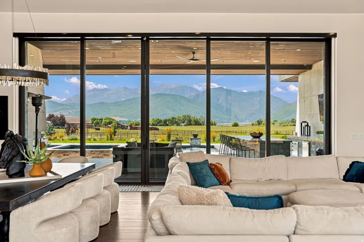 Expansive sliding glass doors, outdoor kitchen with bar seating, integrated pool, and a mountain backdrop