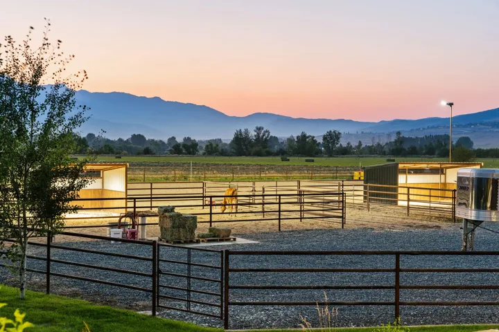 Equine facilities featuring an outdoor arena, permanent fencing, and a covered shelter, all set against a mountain backdrop