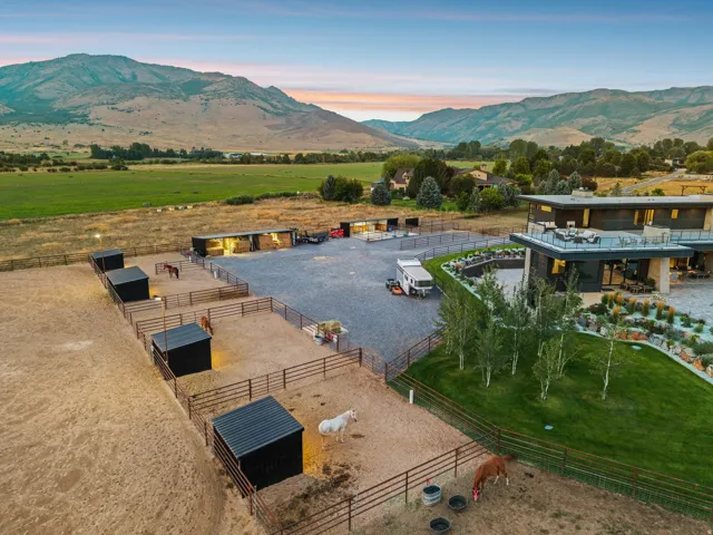 Expansive grounds featuring multiple fenced paddocks and shelters, a gravel driveway, and a contemporary residence with multiple decks