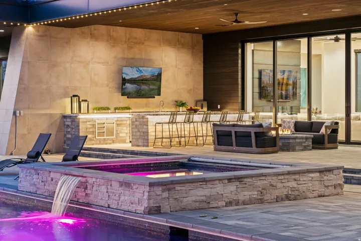 Outdoor living area featuring a built-in bar, integrated fire pit, and a water feature with a spa