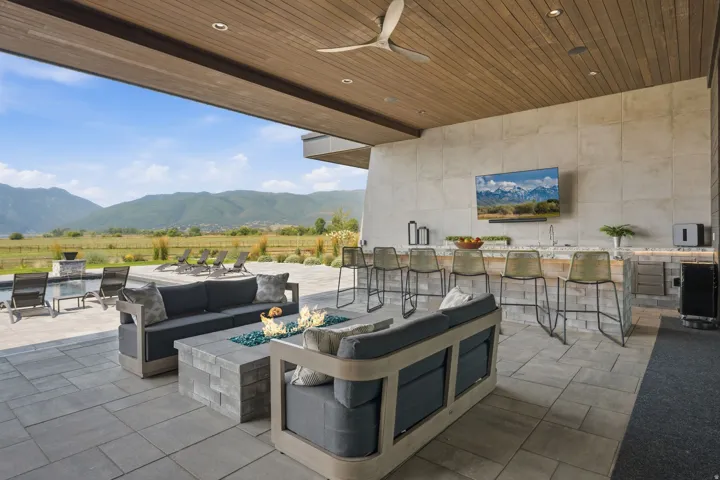 Expansive covered patio featuring a wood-finish ceiling, mounted television, and built-in outdoor kitchen with bar seating