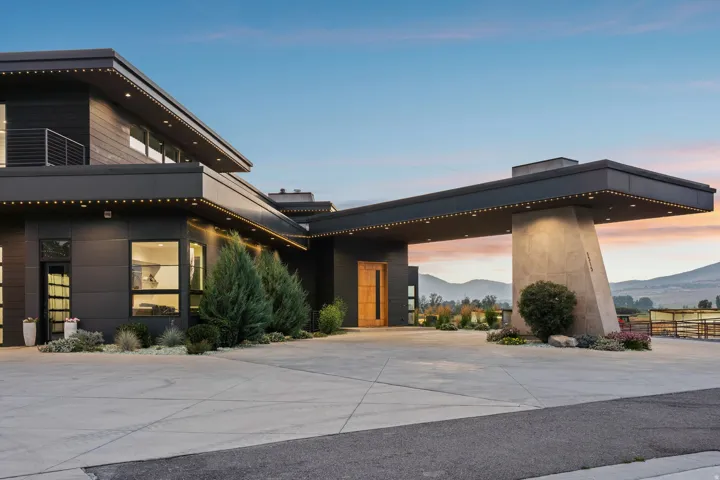 Modern exterior architecture with dark-toned siding, concrete driveway, architectural overhang, and integrated exterior lighting