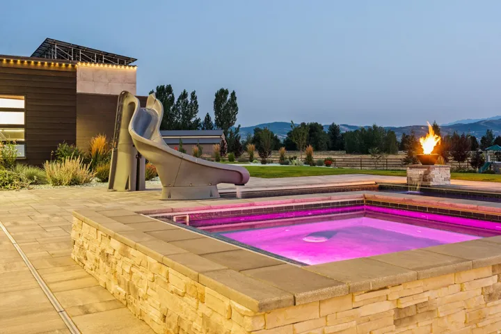 Outdoor spa with stone surround, paver patio, integrated water slide, and fire feature