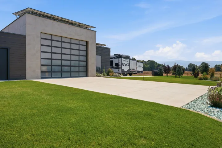 Modern exterior featuring solar panels, a full-view garage door, a concrete driveway, and a manicured lawn