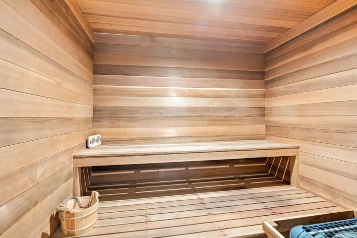 Wood-paneled sauna featuring a built-in bench, slatted wood flooring, and integrated lighting
